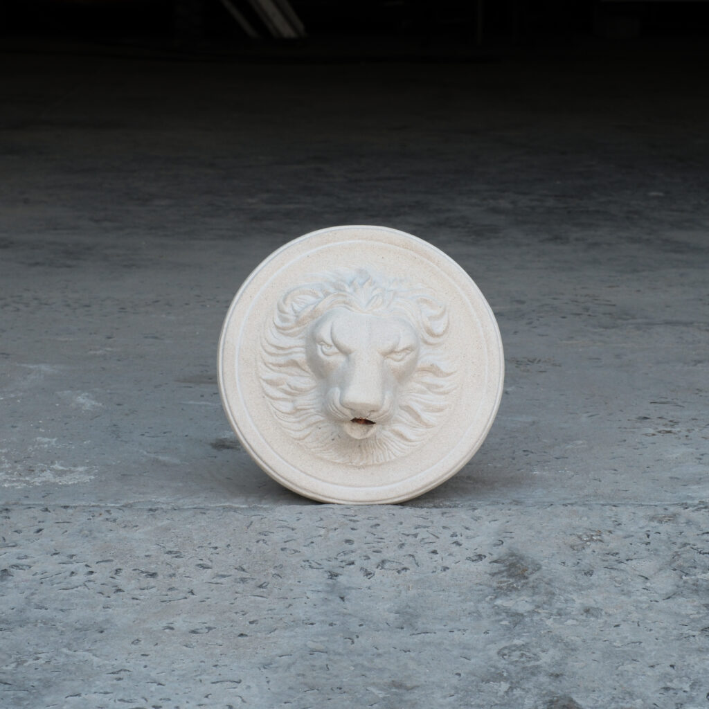 Fountain spout moulded to look like a lion's face set on a disc